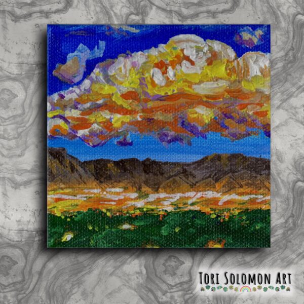 A small colorful painting of a view of Albuquerque in foreground and Sandia Mountains with a colorful cloudy sky