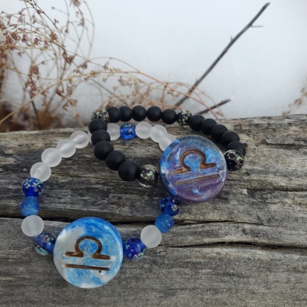 Two bracelets with Libra Zodiac sign charms, on a log.