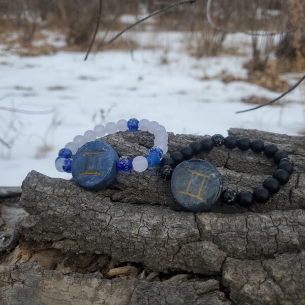 Two bracelets with Gemini Zodiac sign charms, on top of a log.