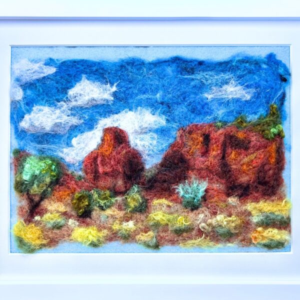 A landscape of red rocks against a blue sky with srubby desert plants in the foreground is made entirely of wool and surruonded by a white frame
