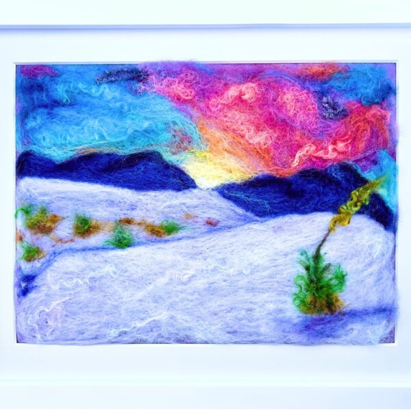 An image of white sand dunes with a colorful sunset in the background and a yucca plant in the foreground made entirely from wool in a white frame